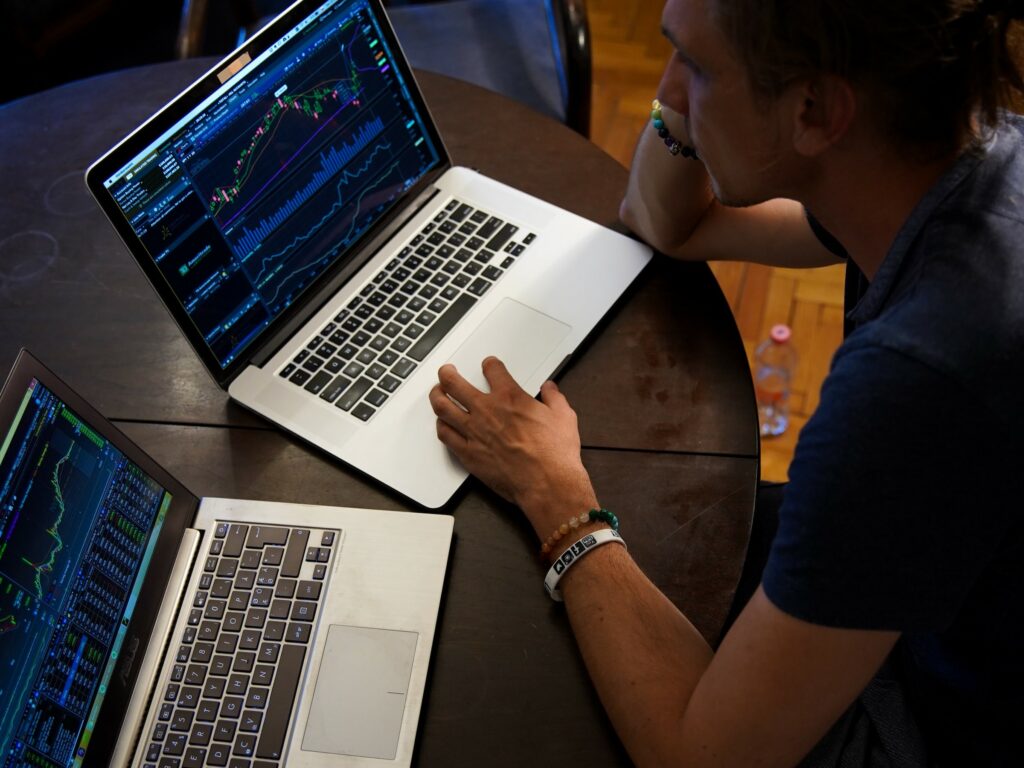 Man looking at financial data on two laptops