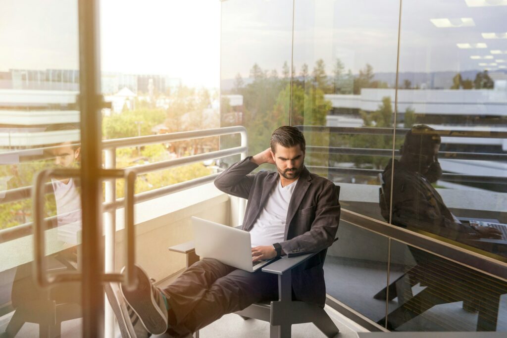Man in blazer sitting on a balcony with a laptop