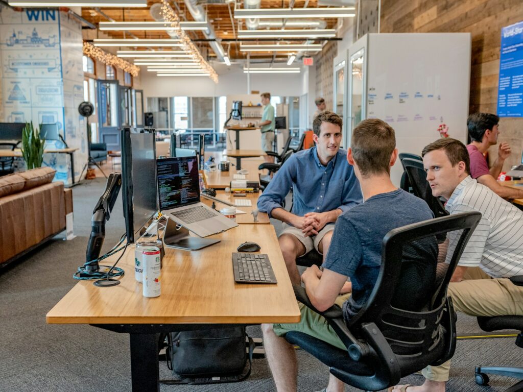 Three men sitting on chairs in front of a desk in an open office