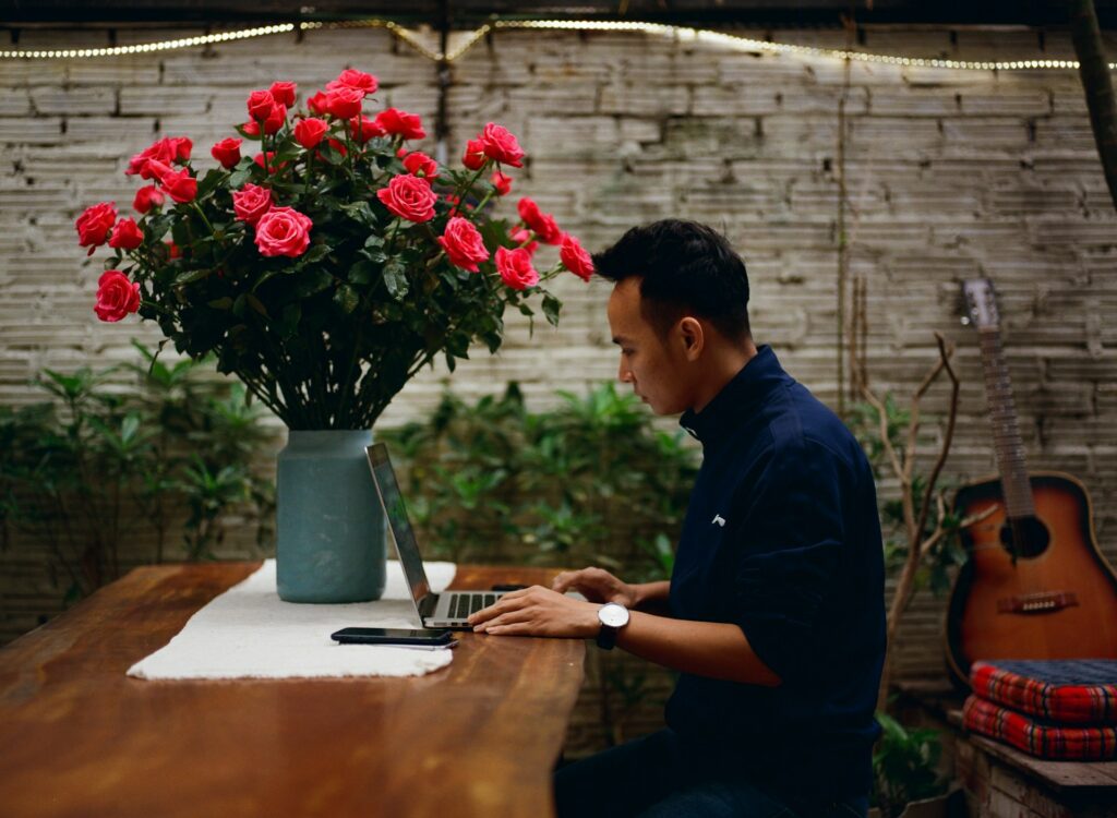 man sitting on chair using laptop for social impact in front of bright flowers