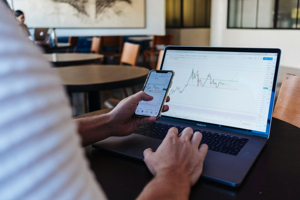 A man looks at financial volatility forecasting graphs on a laptop and smartphone in a cafe