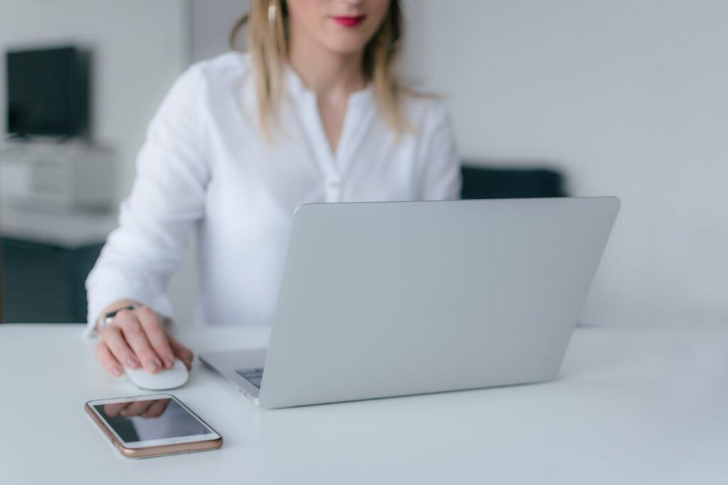 A woman in a white blouse sitting at a white desk and examining the SEC’s AI examination priorities on a laptop