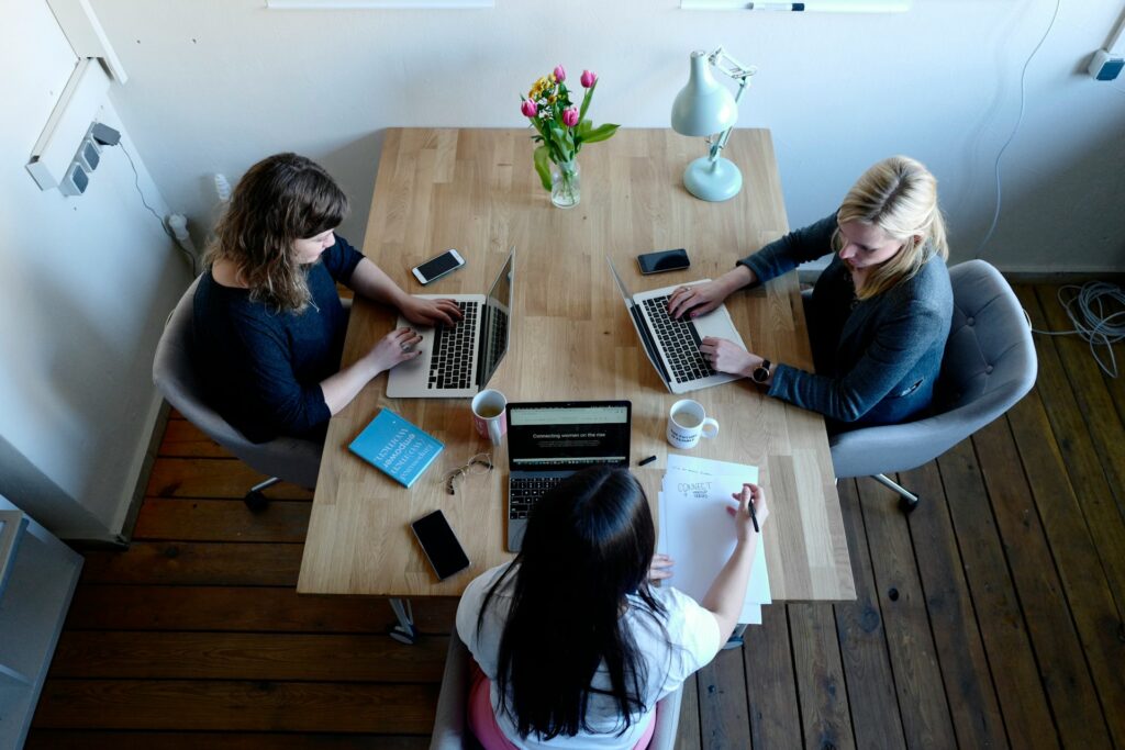 Three women sitting around a table using laptops and discussing AI regulations