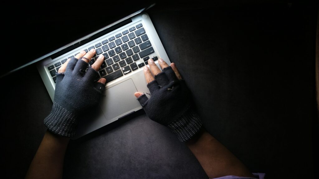 gloved hands touching laptop keyboard in a dark room representing dark web monitoring