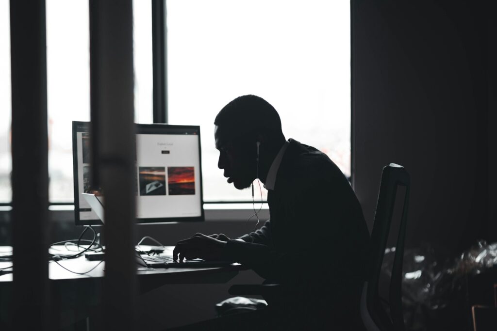 A professional, frustrated due to outages, works at his desk in a dark office.