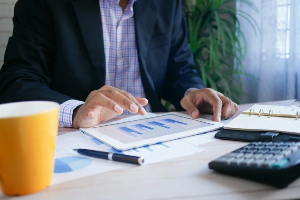 Image of a man in a blazer using a unified communicaitons platform on a tablet while sitting at a white desk.