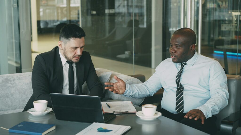 Well-dressed men sit in a business lounge with laptops discussing AI readiness in financial services.