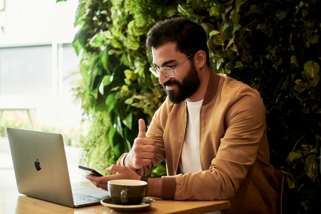 A man connecting to cloud-native architecture on his mobile and laptop gives a thumbs up.