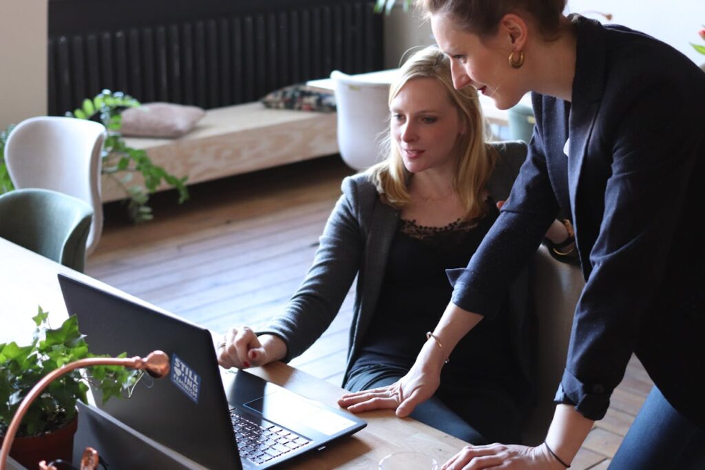 Two professional women look at measurements of AI in financial services on a laptop in an office.