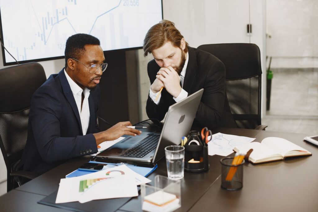 Two colleagues analyze their firm's AI skills gap at a laptop in a conference room.