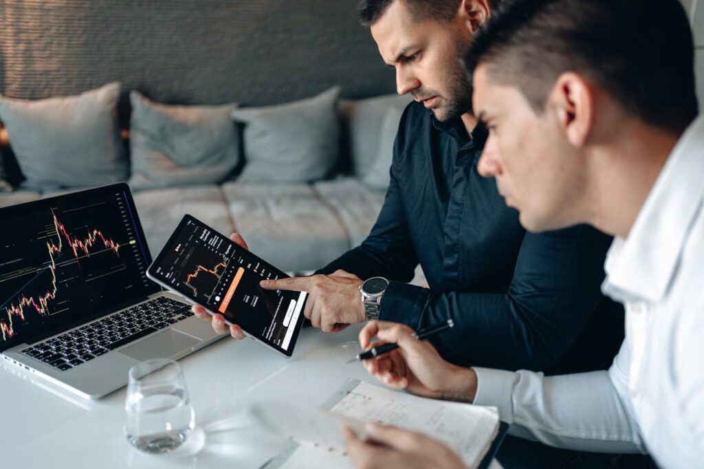 Two colleagues engage in human oversight of AI at a shared table, looking at a laptop and tablet displaying data.