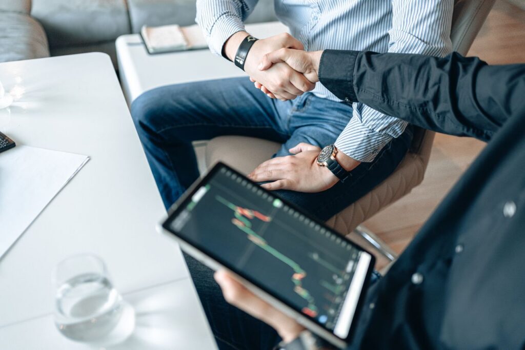 Men shake hands while sitting in an office, looking at a chart on a tablet signifying non-human identity security.