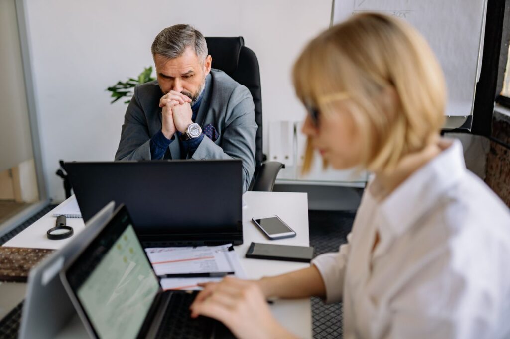 Two professionals with laptops manage AI-driven cloud security in a brightly-lit office.