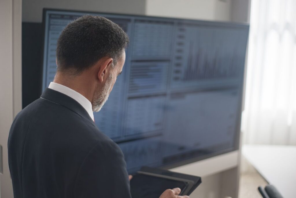 Businessman engaging in disaster recovery for investment firms using a tablet and an enormous screen with charts.